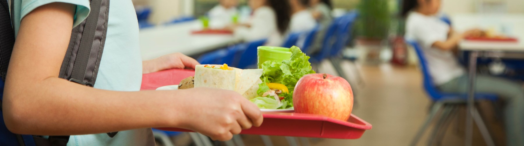 student carrying a lunch tray with a sandwich and apple through the a school cafeteria